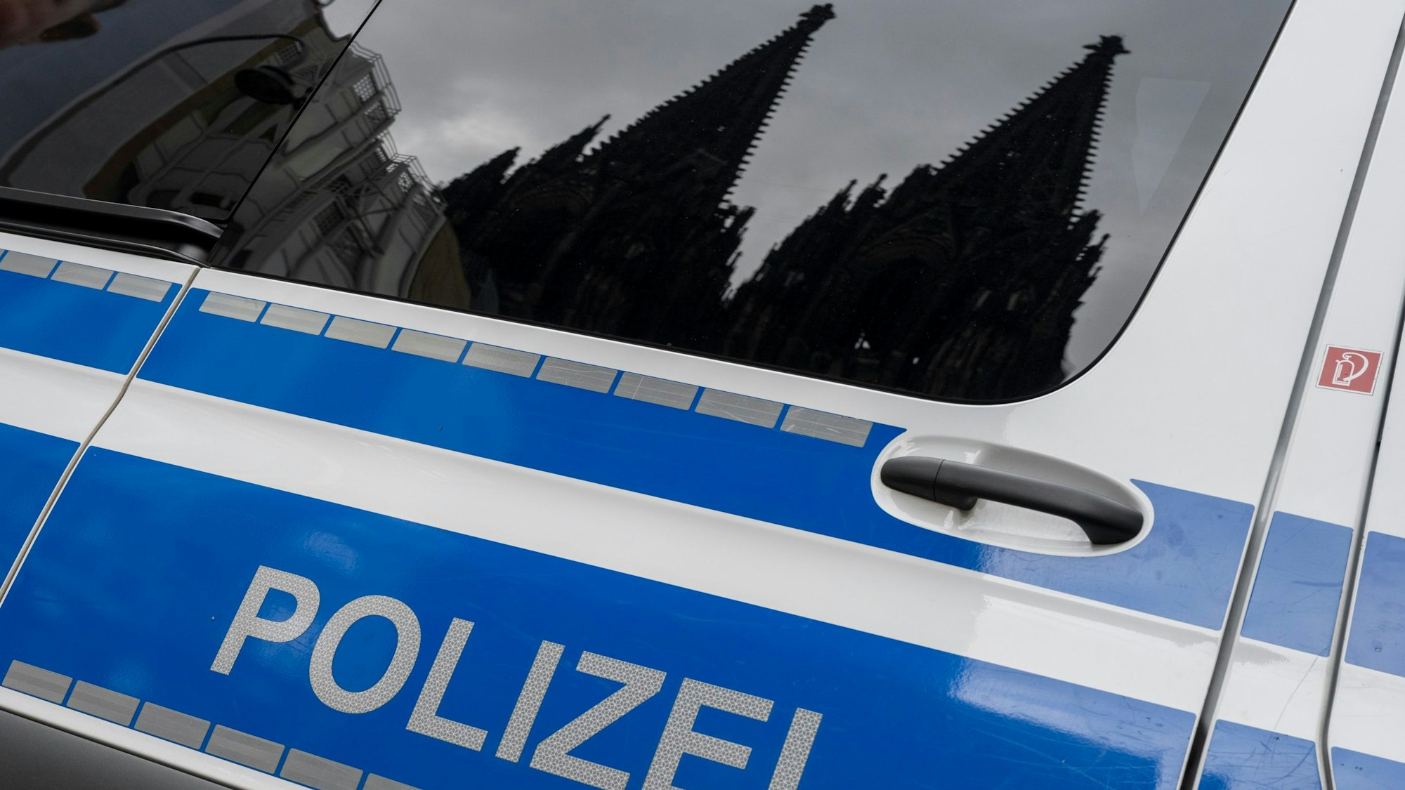 Der Kölner Dom spiegelt sich im Fenster eines Polizeifahrzeugs.