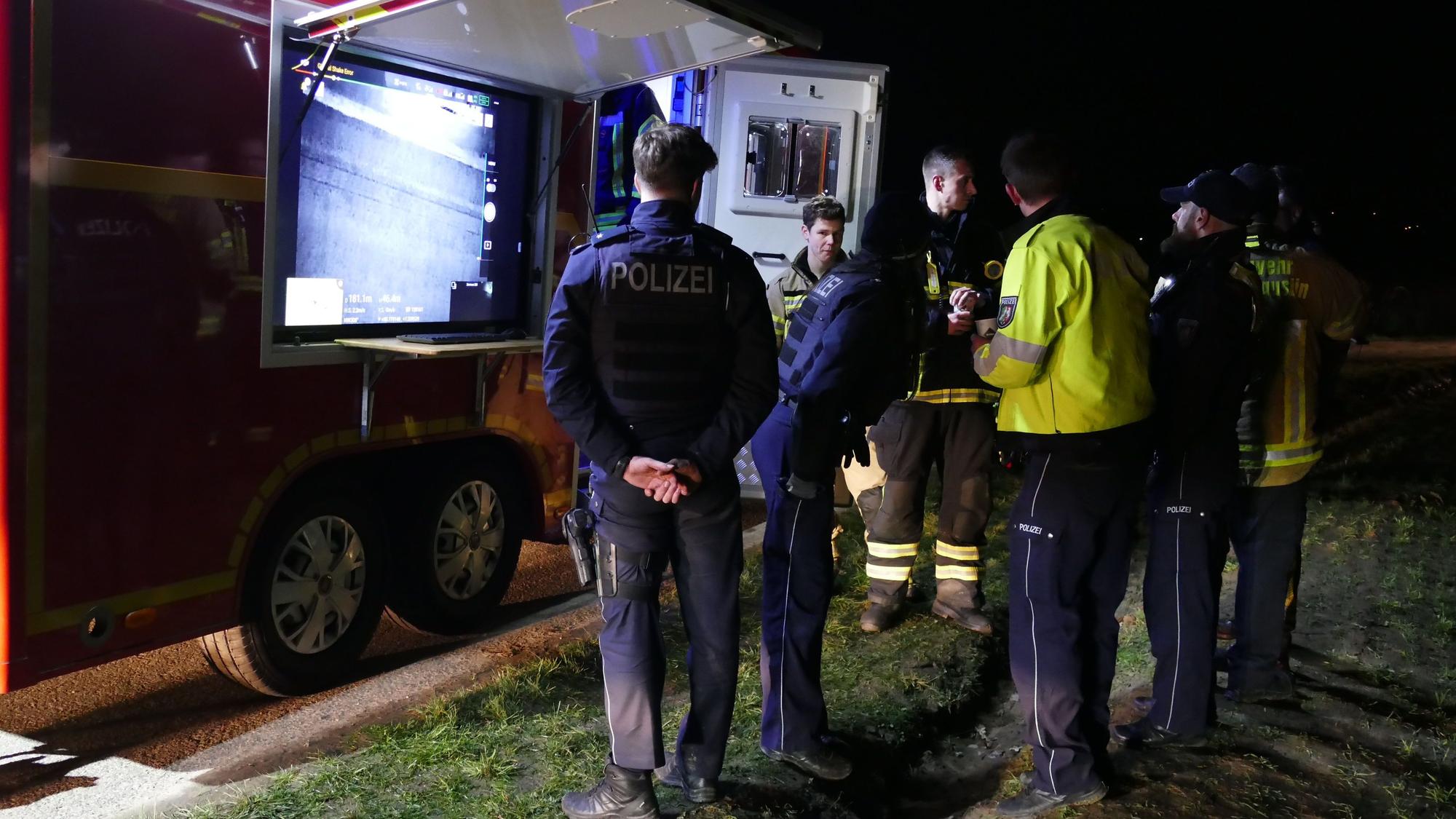 Polizisten und Feuerwehrleute stehen vor einem Feuerwehr-Fahrzeug mit Bildschirm.