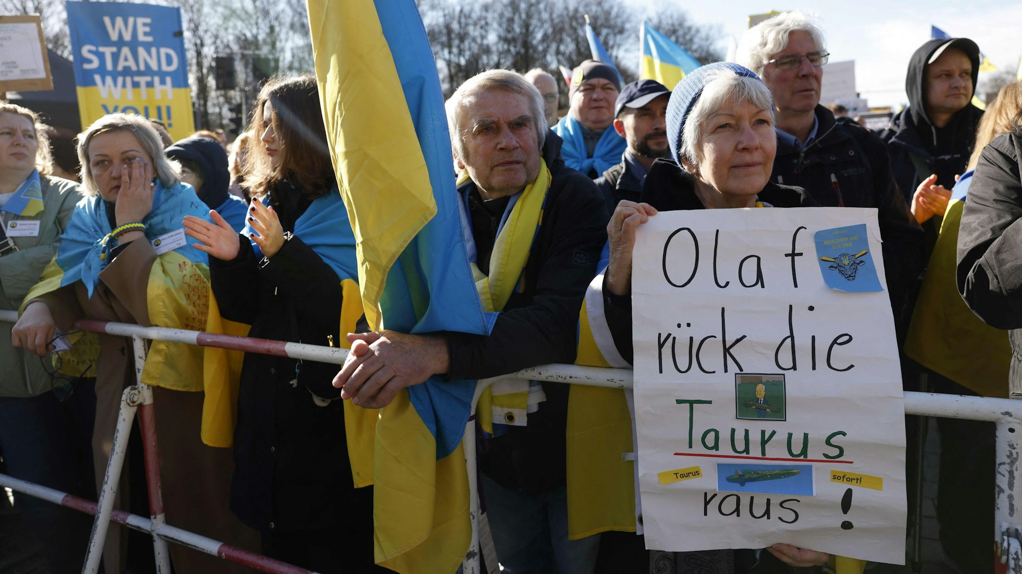 Anlässlich des Jahrestags des Angriffs Russlands auf die Ukraine am 24. Februar hält eine Teilnehmerin der Berliner Solidaritätskundgebung für die Ukraine ein Plakat mit der Aufschrift „Olaf, rück die Taurus raus!“ Viele Teilnehmer haben sich die gelb-blaue Flagge der Ukraine umgebunden.