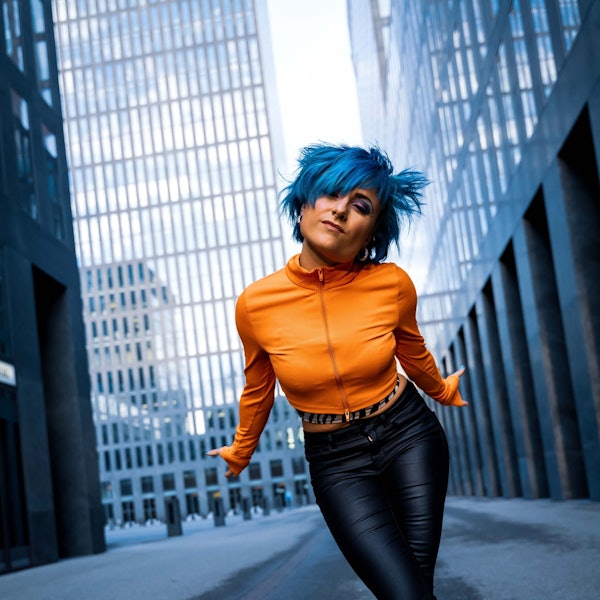 Eine junge Frau mit blauen Haaren guckt herausfordernd in die Kamera.