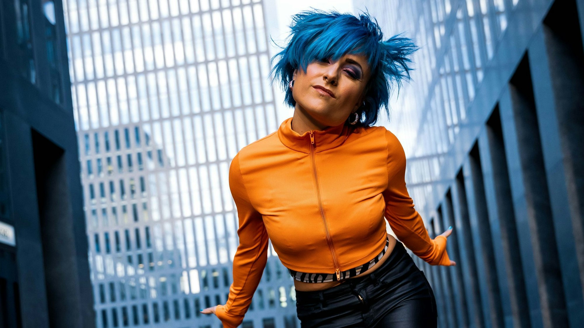 Eine junge Frau mit blauen Haaren guckt herausfordernd in die Kamera.