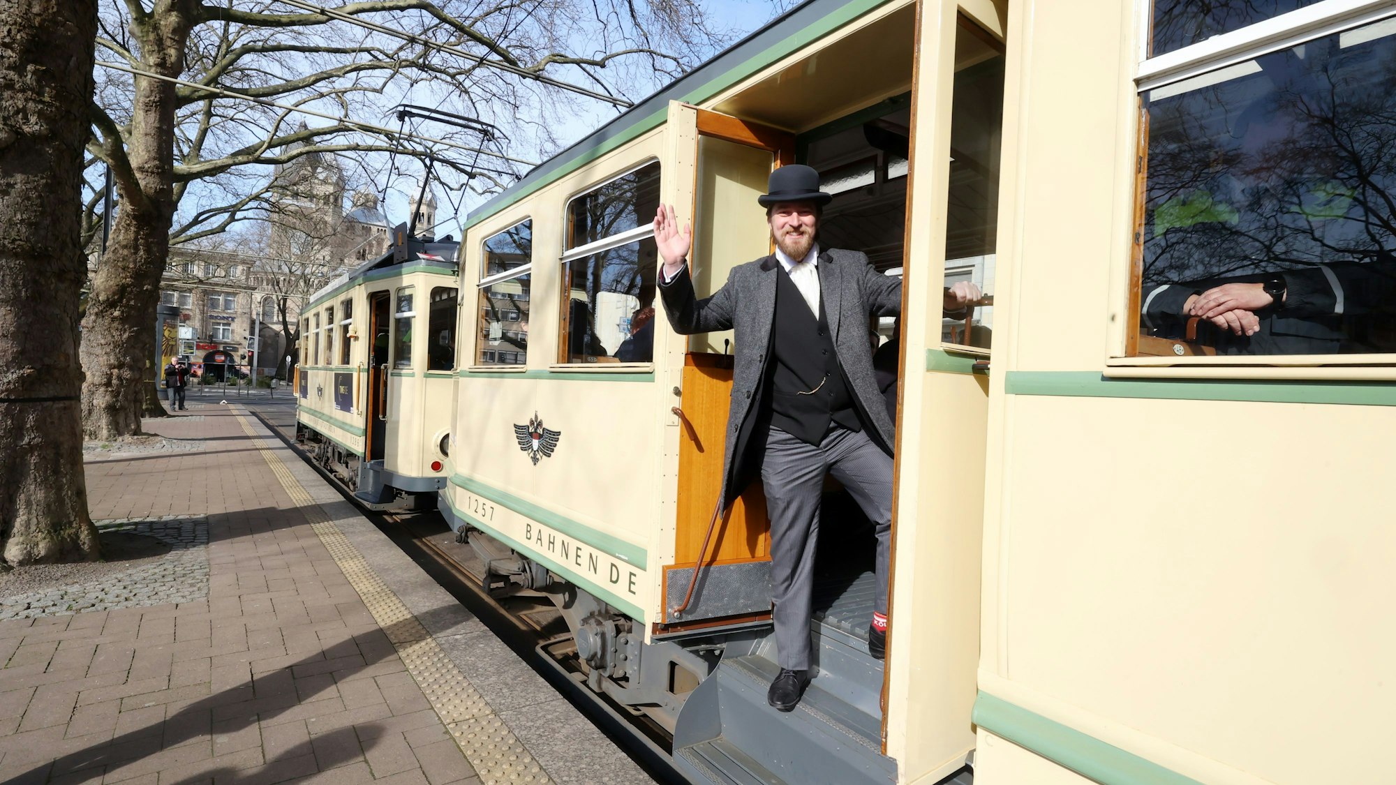 Ein Mann winkt aus einer historischen Straßenbahn heraus