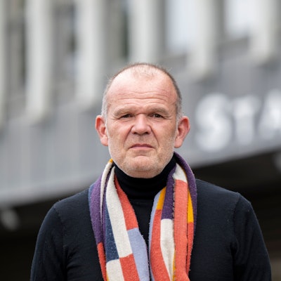 François-Xavier Roth steht vor dem Staatenhaus. Er trägt einen bunten Schal.