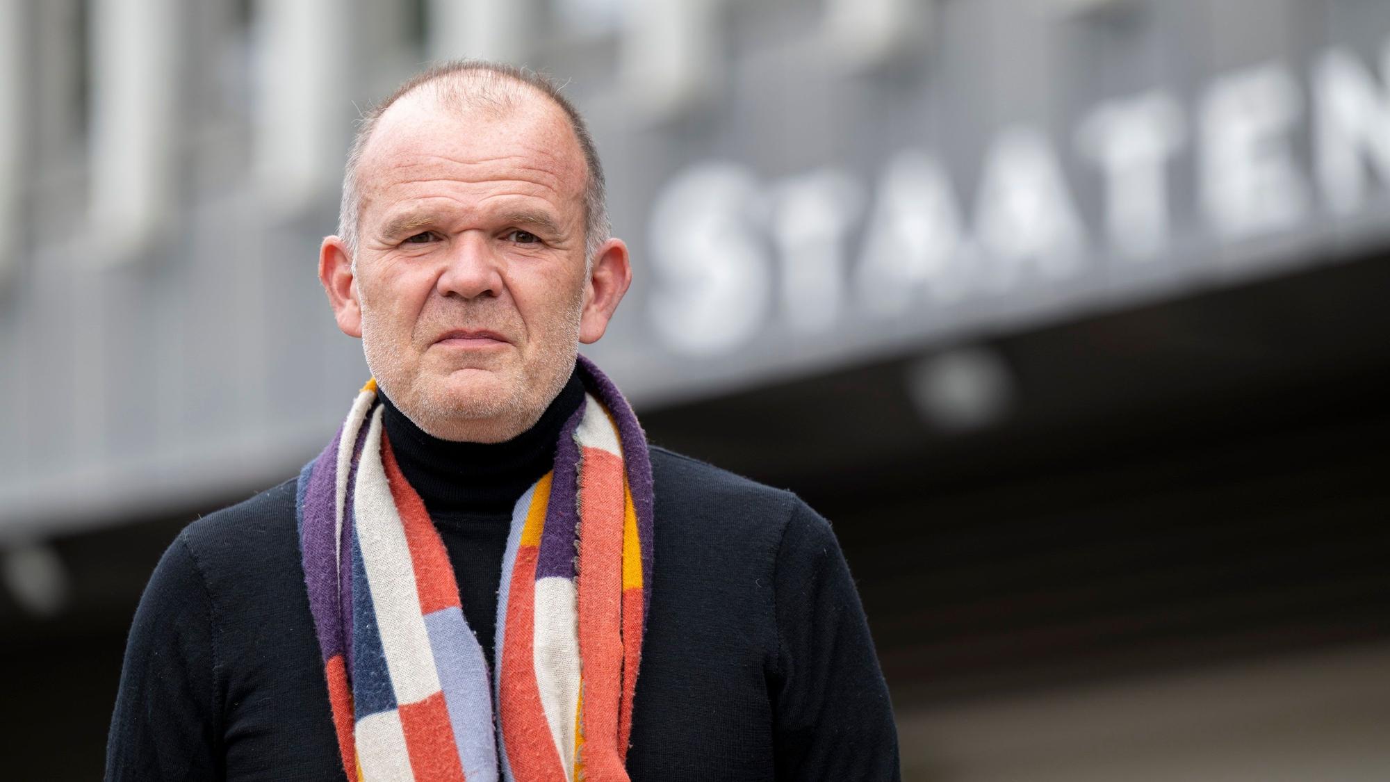 François-Xavier Roth steht vor dem Staatenhaus. Er trägt einen bunten Schal.