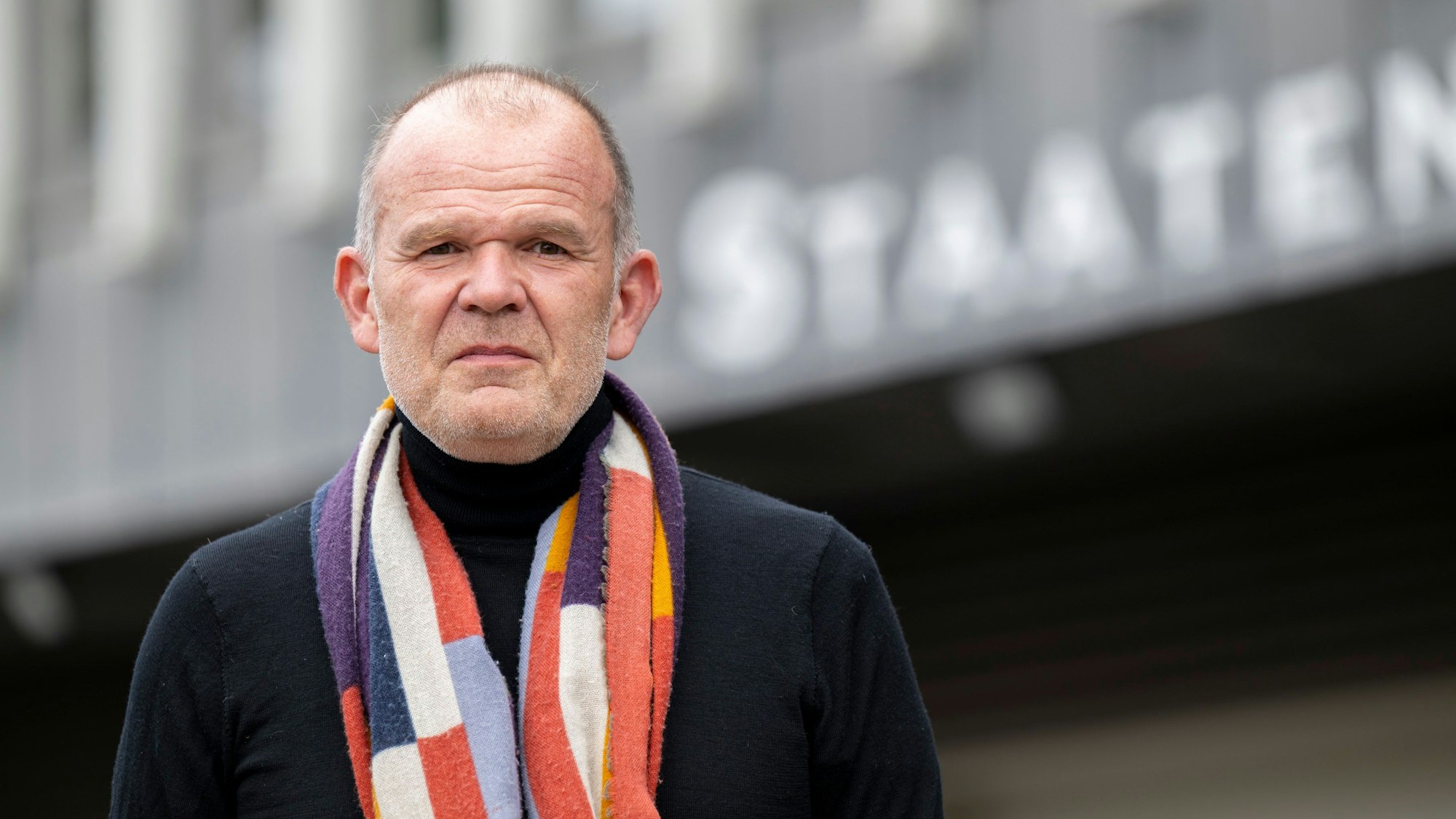 François-Xavier Roth steht vor dem Staatenhaus. Er trägt einen bunten Schal.