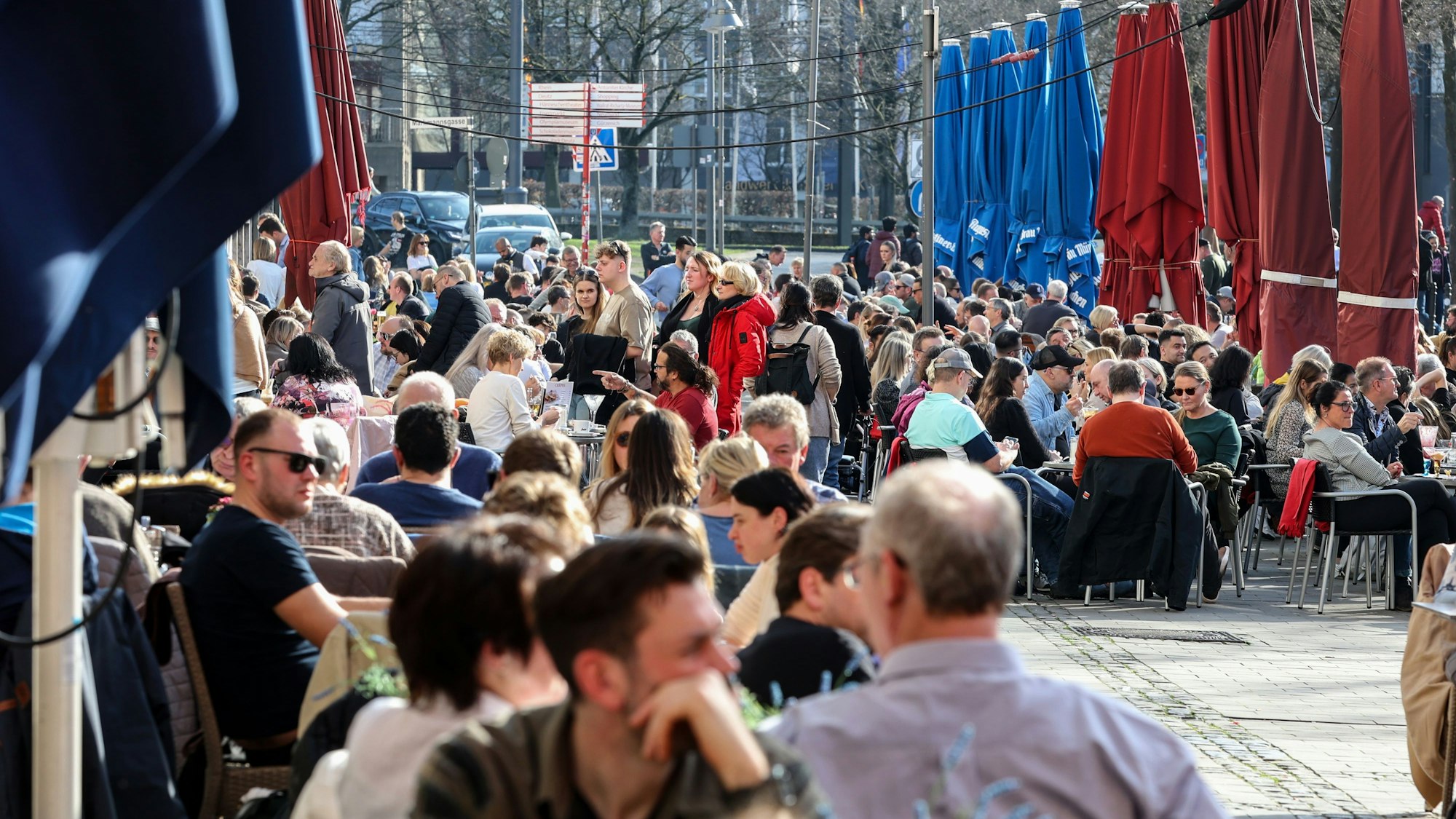 Menschen sitzen in der Außengastronomie eines Cafés in der Sonne.