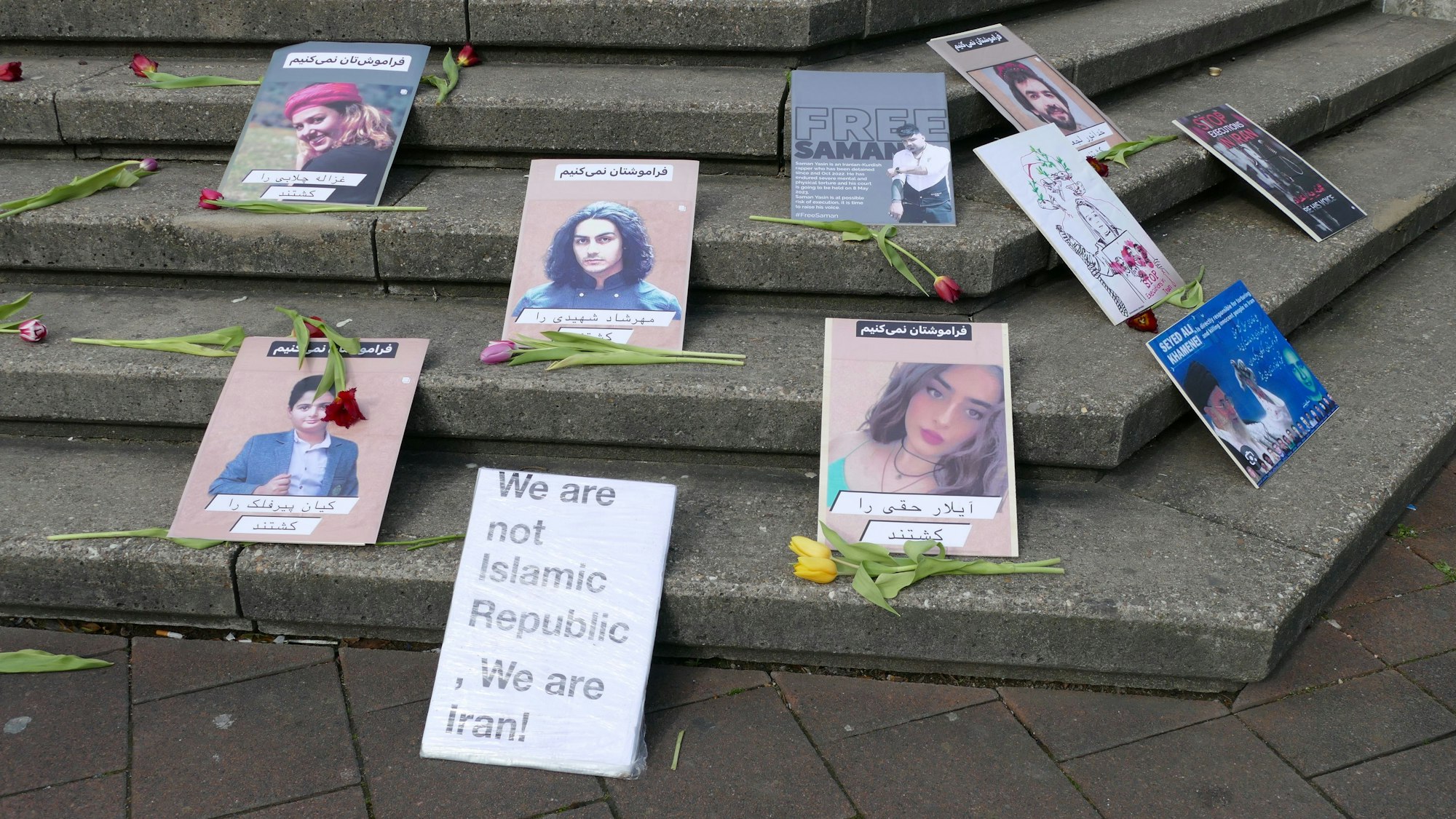 Fotos von Männern und Frauen liegen auf Treppenstufen, dazwischen liegen Blumen.