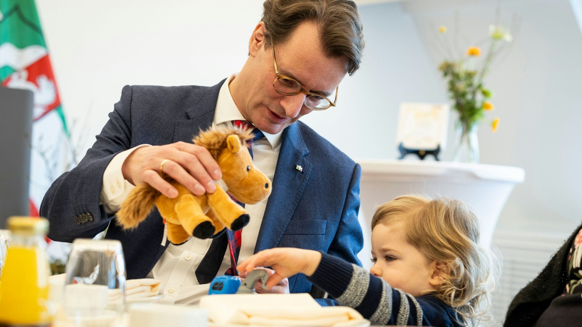 Hendrik Wüst (CDU, li), Ministerpräsident von Nordrhein-Westfalen, spielt am Tisch mit seinem Ehrenpatenkind Daniel.