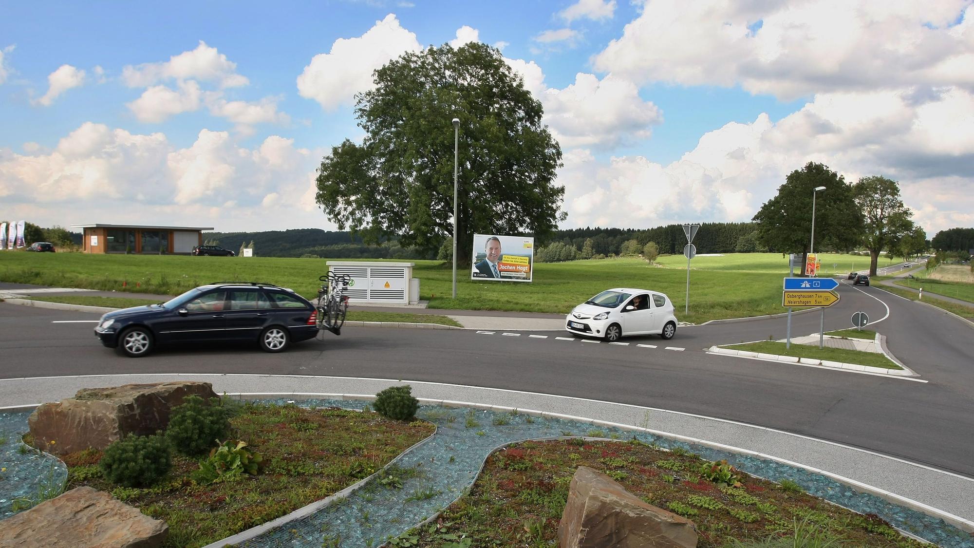 Ein Kreisverkehr und Autos im Vordergrund, dahinter eine große Wiese.
