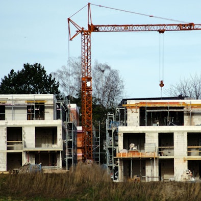 Ein Rohbau ohne Fenster, daneben ein Kran vor blauem Himmel.