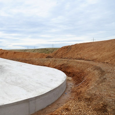 Drei Männer in Schutzkleidung stehen auf einem riesigen Fundament.