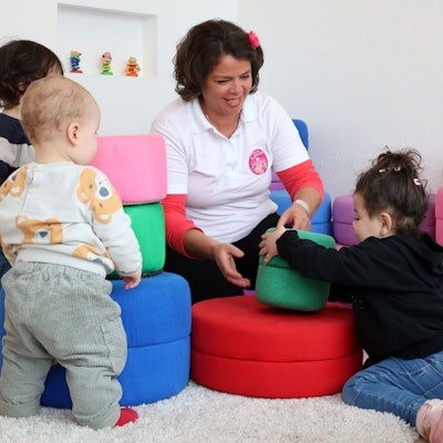 Eine Kindertagespflegerin spielt mit drei Kleinkindern.