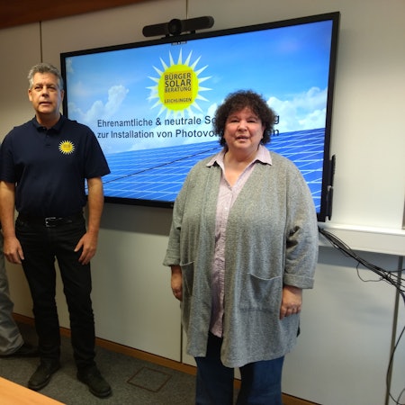 Zwei Männer und eine Frau stehen vor einem Bildschirm.