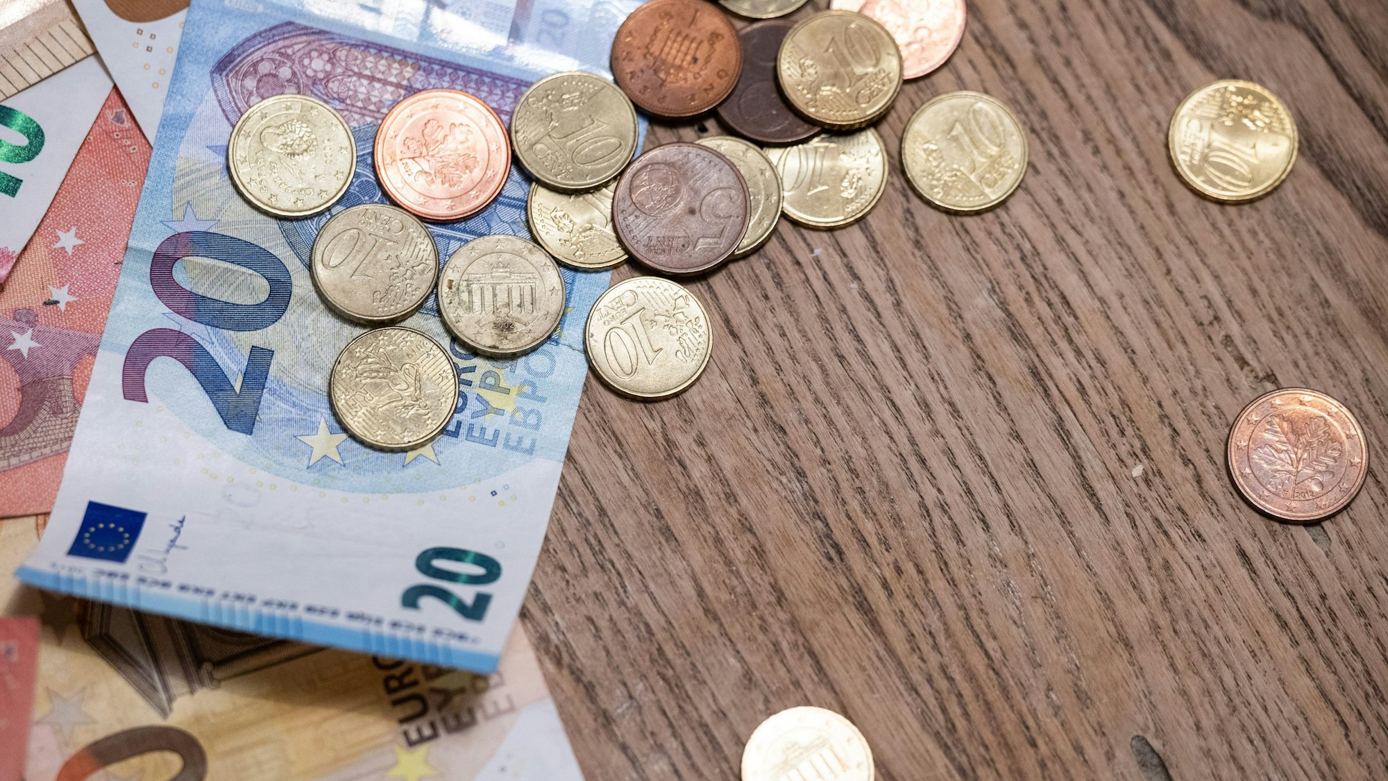 Münzen und Geldscheine liegen auf einem Holztisch.