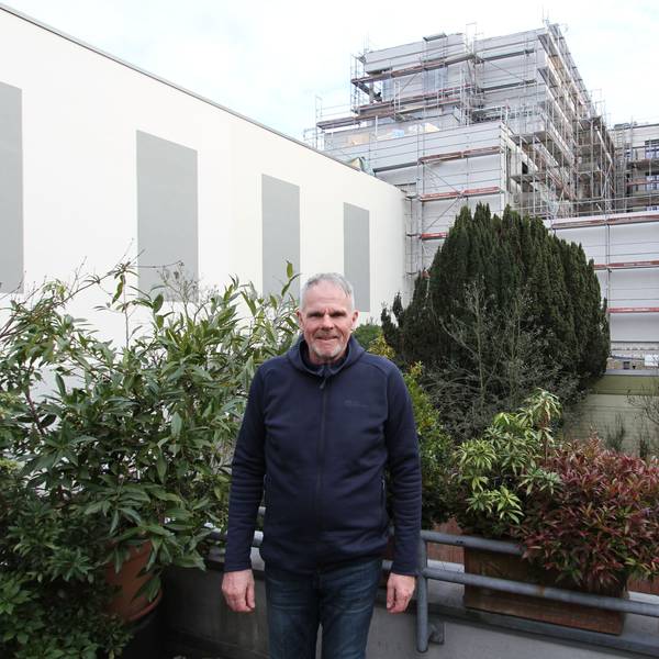 Ein Mann auf einem bepflanzten Balkon vor einem großen Wohngebäude