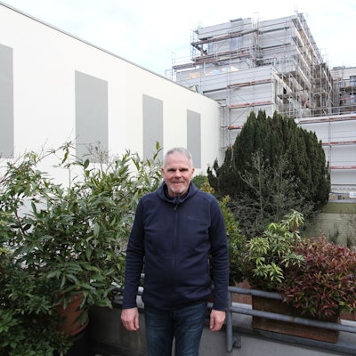 Ein Mann auf einem bepflanzten Balkon vor einem großen Wohngebäude