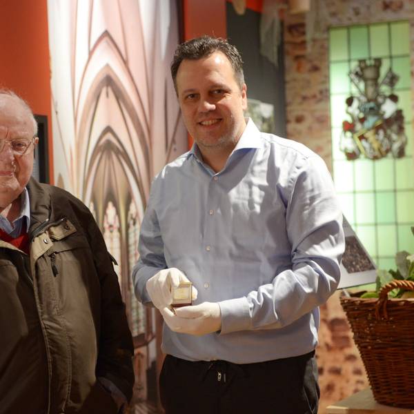 Rolf Müller-Blagovich und Sacha Reichelt stehen im Stadtmuseum Euskirchen. Reichelt zeigt eine der Münzen, die Müller der Stadt geschenkt hat.