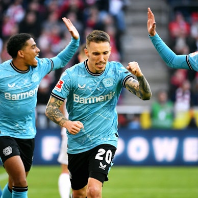 Alejandro Grimaldo (m.) jubelt nach seinem Tor zum 0:2 gegen den 1. FC Köln. Hinter ihm sind Amine Adli (l.) und Borja Iglesias (r.) im Begriff, mit Händen einzuschlagen.