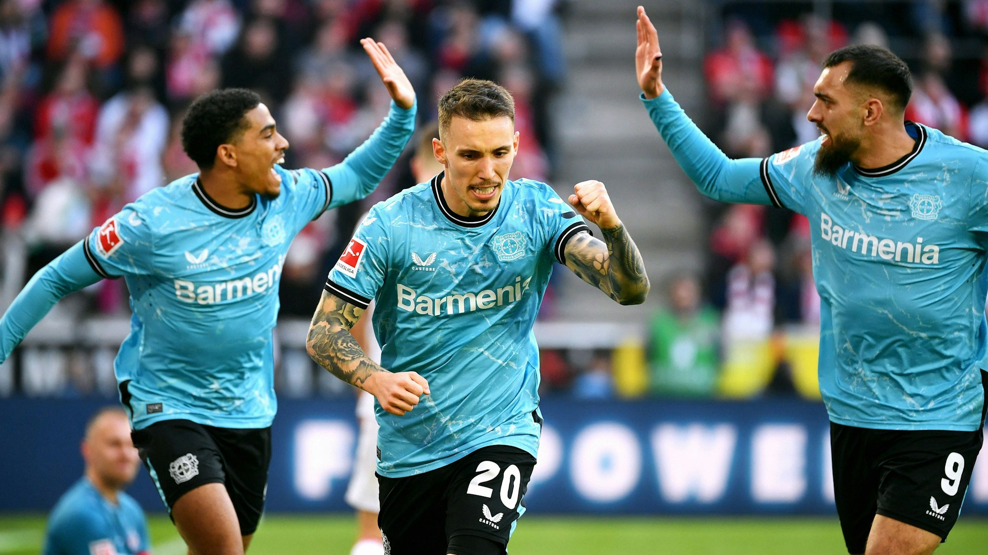 Alejandro Grimaldo (m.) jubelt nach seinem Tor zum 0:2 gegen den 1. FC Köln. Hinter ihm sind Amine Adli (l.) und Borja Iglesias (r.) im Begriff, mit Händen einzuschlagen.