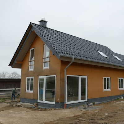 Ein Einfamilienhaus auf einem Baugrundstück. Das vordere Haus ist fertig, an zwei weiteren im Hintergrund wird noch gebaut.