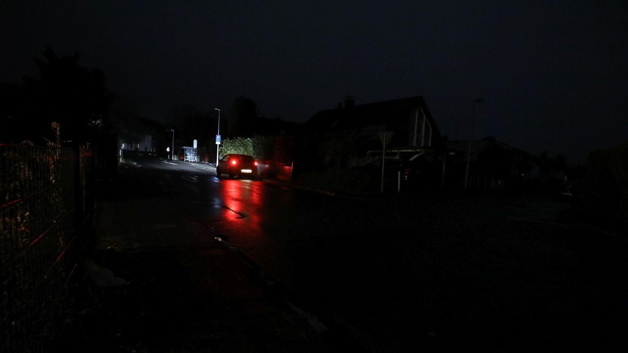 Ein Auto fährt über eine sehr dunkle Straße, die nur durch die Scheinwerfer beleuchtet wird.