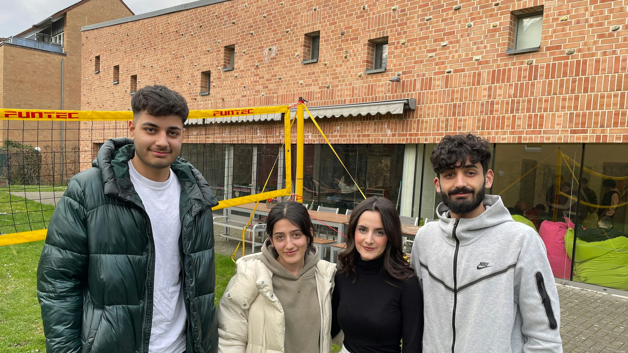 Die Besucherinnen und Besucher des Rondorfer Jugendzentrums „eins2null'“ Hamada(19), Sedra (20), Janaman (17) und Hadi (22) (von links) stehen vor dem Gebäude mit großen Glasfassaden.
