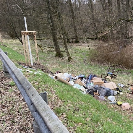 Ein Sperrmüllhaufen liegt auf einer Wiese hinter einer Leitplanke.