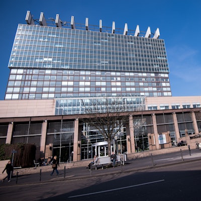 Zu sehen sind das Bettenhaus der Kölner Uniklinik und ein Rettungswagen in der Vorderansicht.