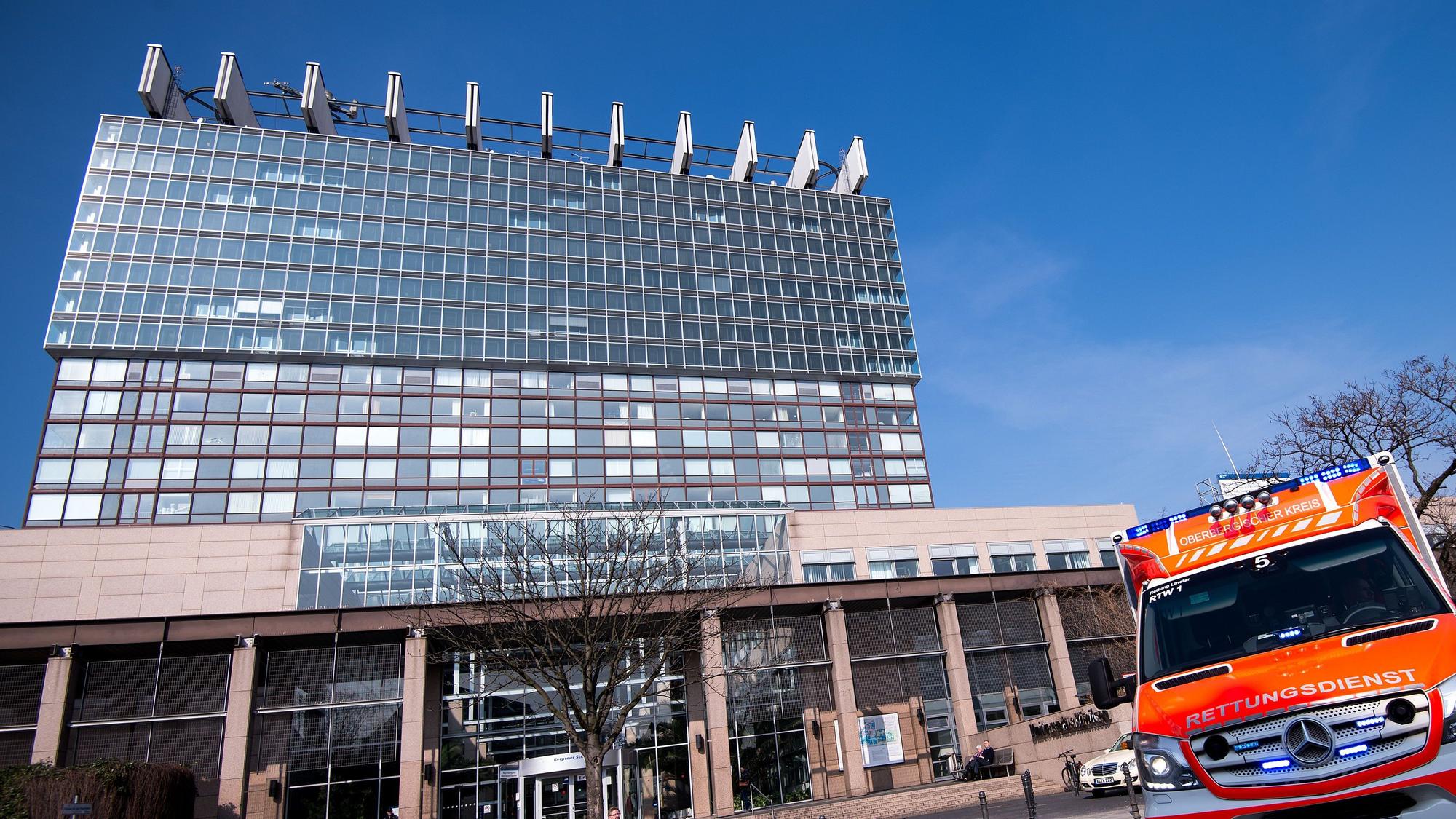 Zu sehen sind das Bettenhaus der Kölner Uniklinik und ein Rettungswagen in der Vorderansicht.