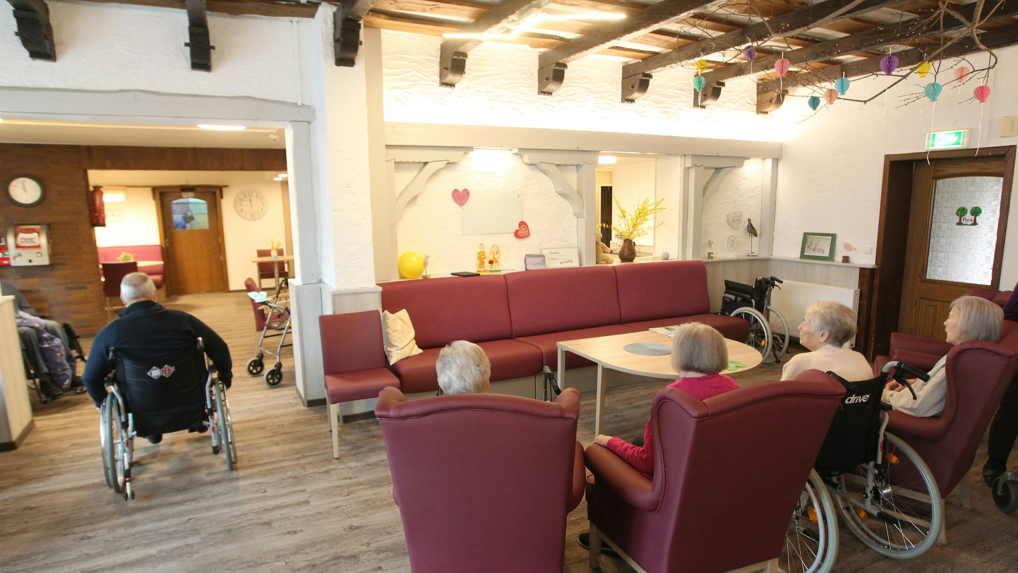 Das Bild zeigt Seniorinnen und Senioren in Sesseln und Rollstühlen in einem Gemeinschaftsraum.