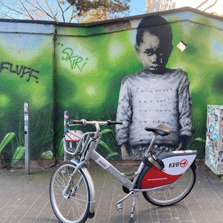 Eine Wandmalerei zeigt einen trotzig blickenden kleinen Jungen vor grünem Hintergrund.