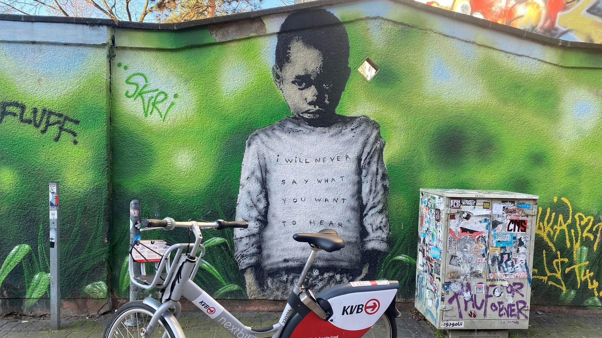 Eine Wandmalerei zeigt einen trotzig blickenden kleinen Jungen vor grünem Hintergrund.