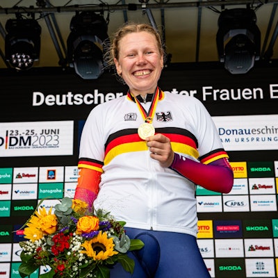 Mieke Kröger hält bei einer Siegerehrung ihre Goldmedaille in die Luft und lächelt.