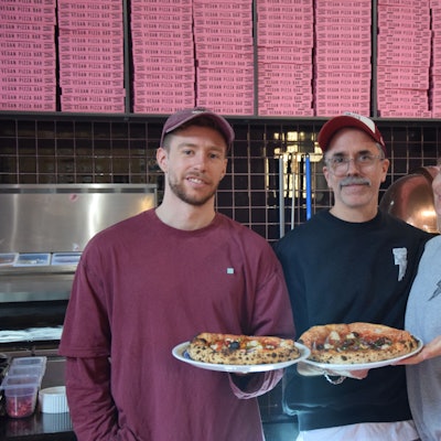 Zu sehen sind Mitchell Weiser, Ingo Noack und Verena Malta, die zwei Pizzen in die Kamera halten.