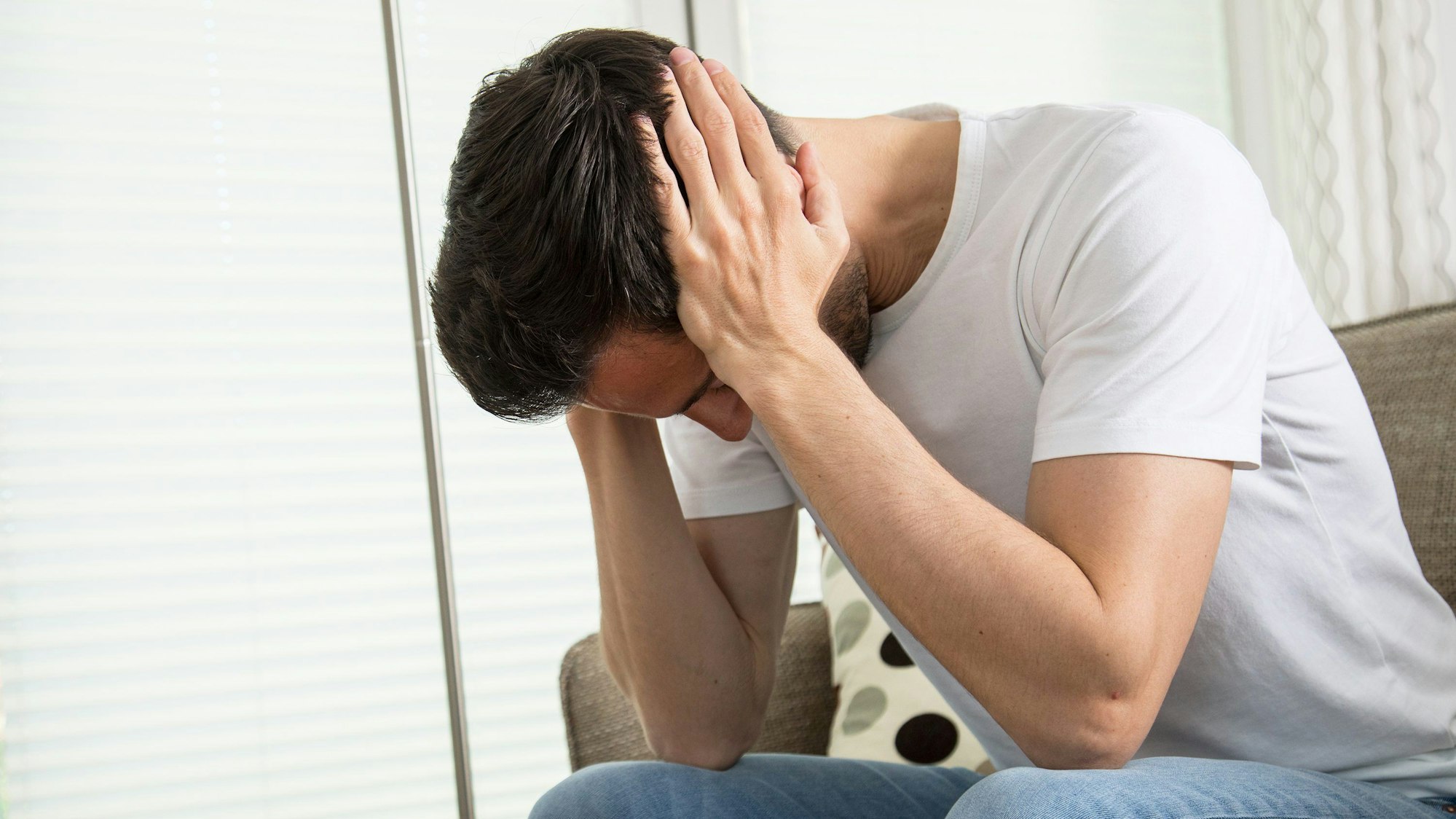 Eine Junge auf dem Sofa hält sich die Hände vor das Gesicht.