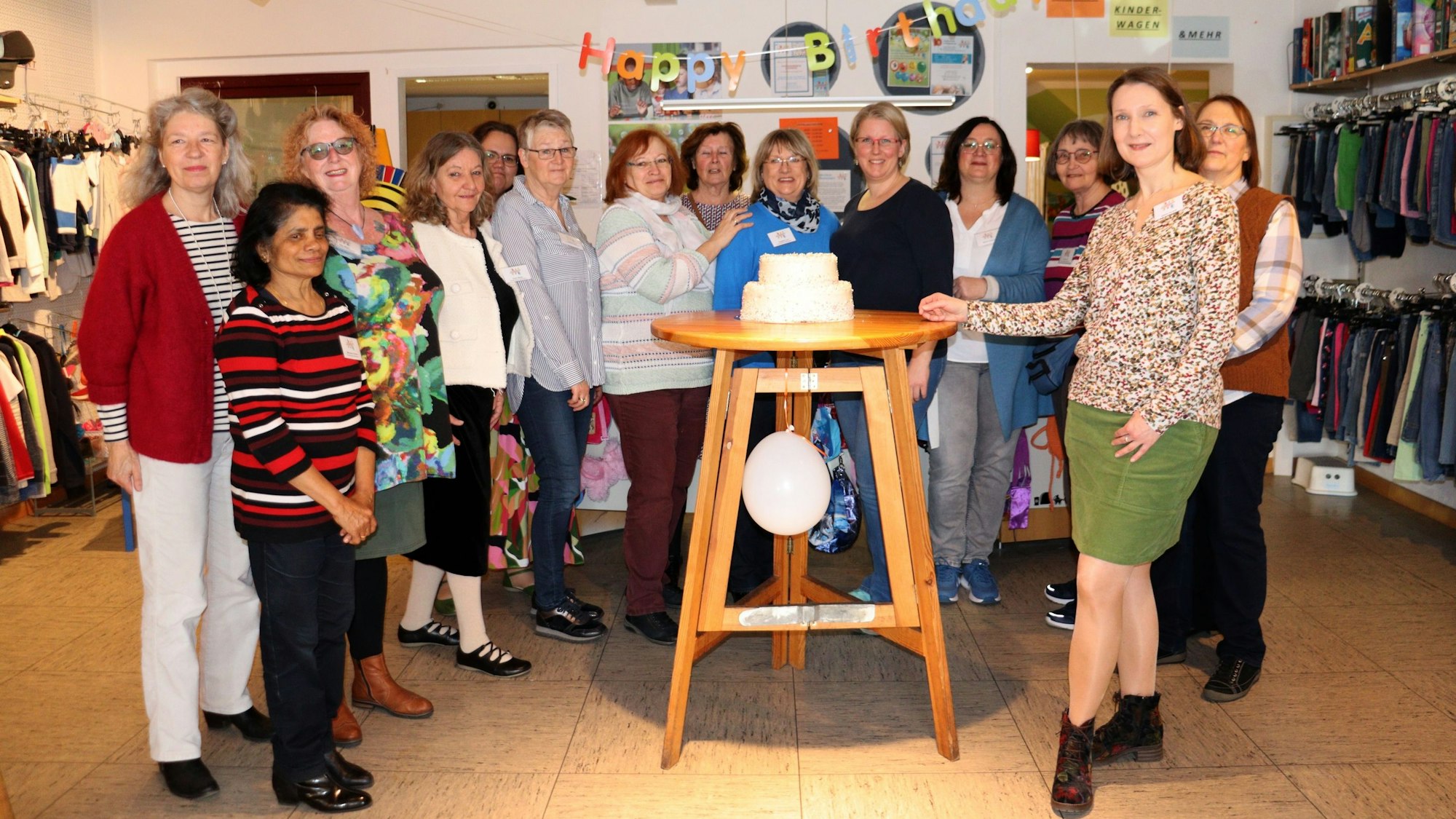 Viele Frauen stehen im Halbkreis um einen Stehtisch mit einer Geburtstagstorte darauf.