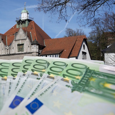 Die Fotomontage zeigt im Vordergrund ein Bündel von 100 Euro-Scheinen, im Hintergrund ist das historische Rathaus zu sehen.