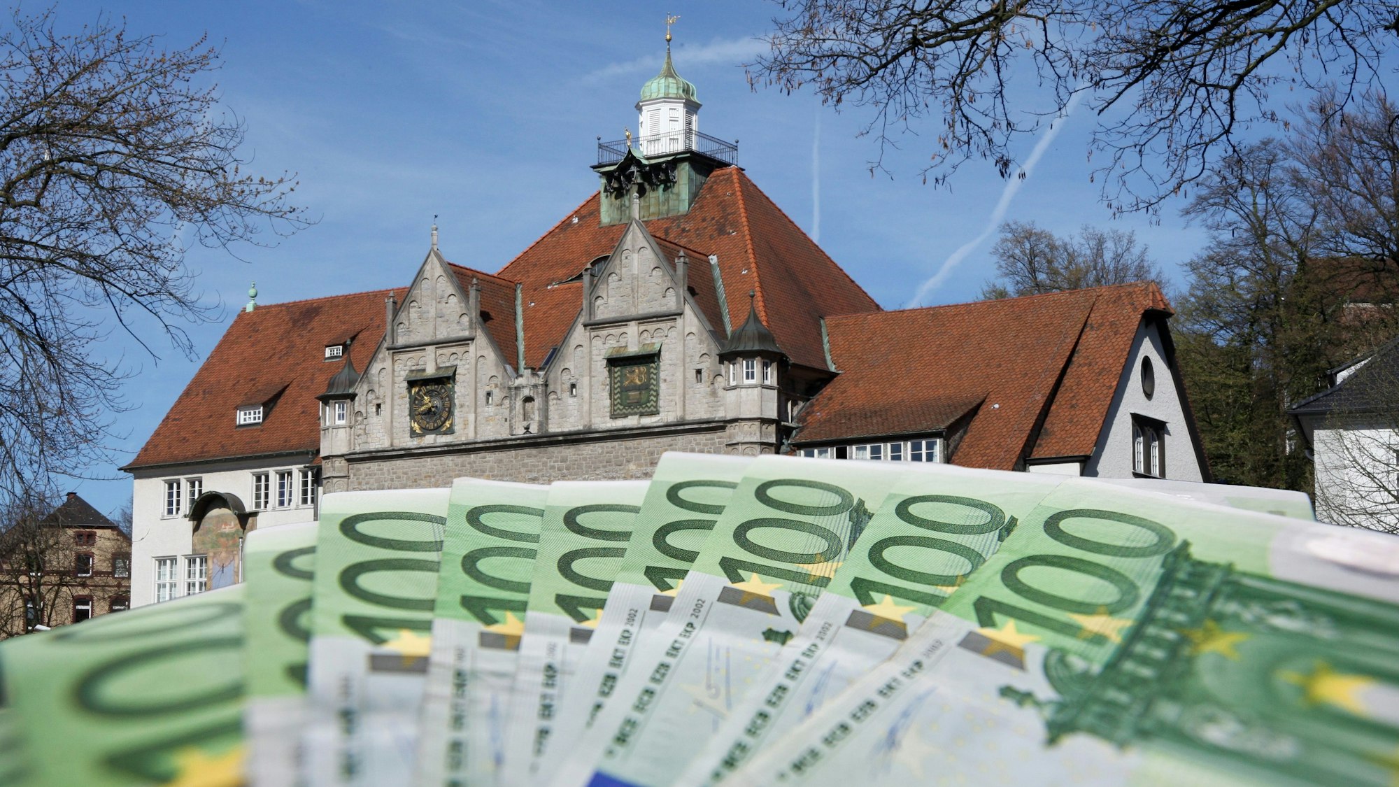 Fotomontage zeigt Geldscheine im Vordergrund, das Rathaus im Hintergrund.