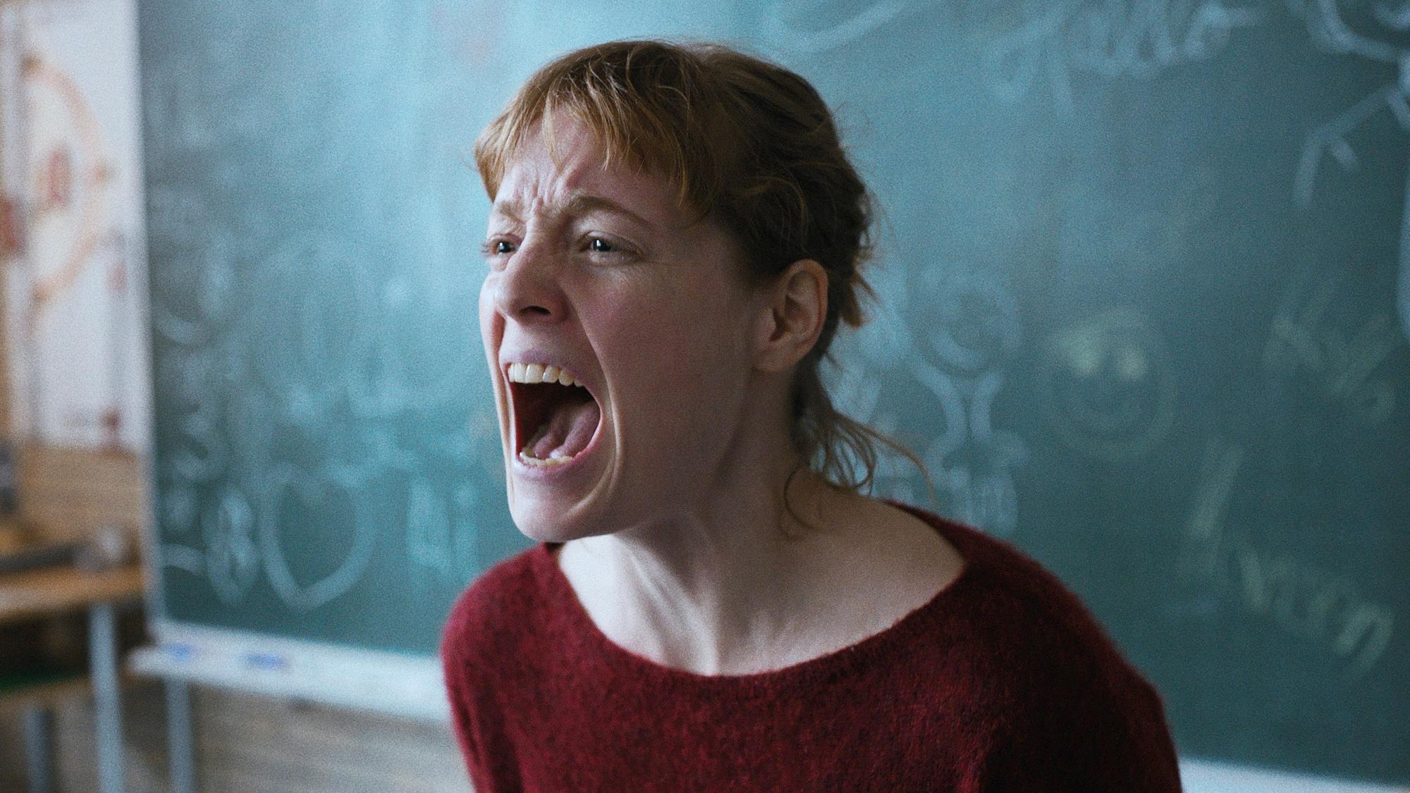 Eine junge Lehrerin steht schreiend vor der Schultafel.