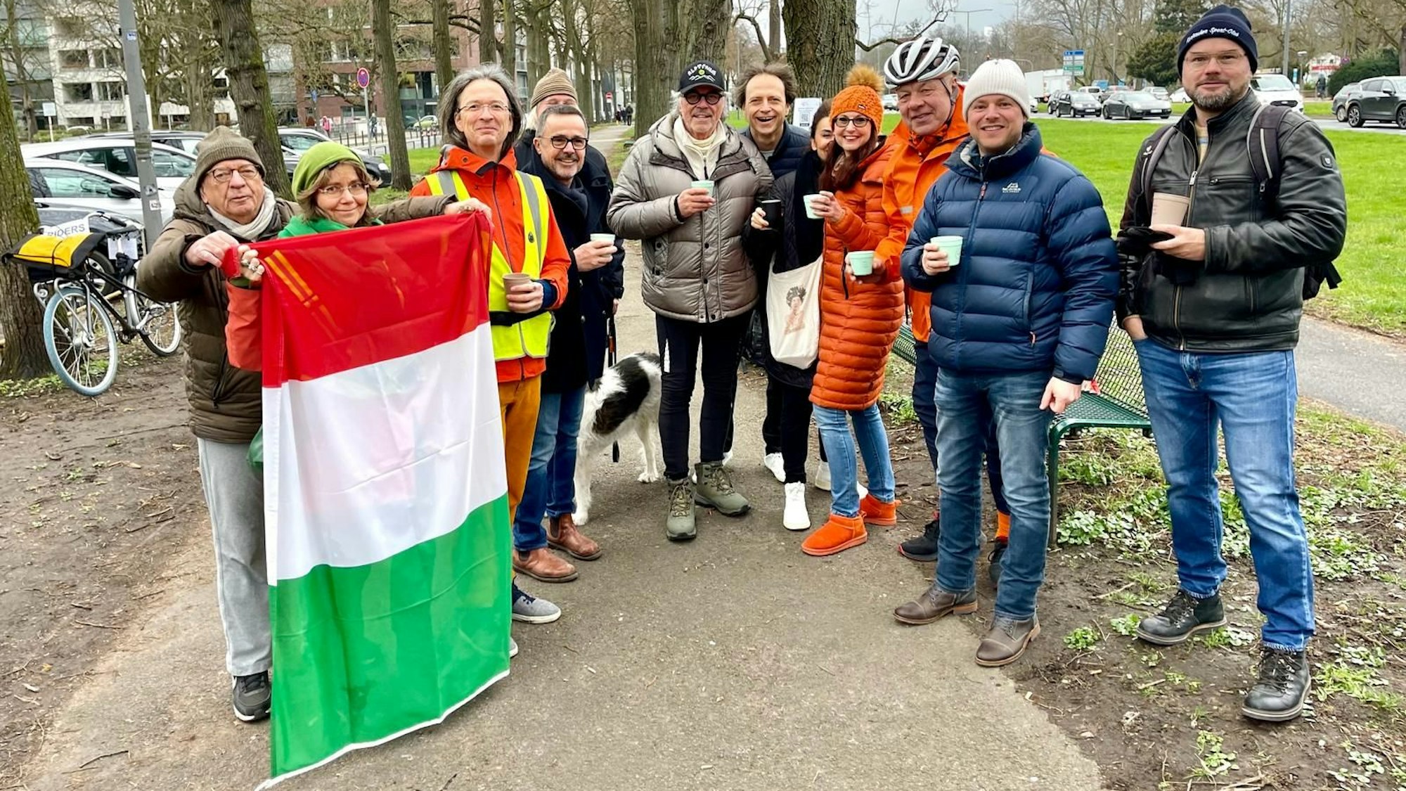 Eine Gruppe Menschen steht im Halbkreis auf einem Weg an einer Grünfläche.