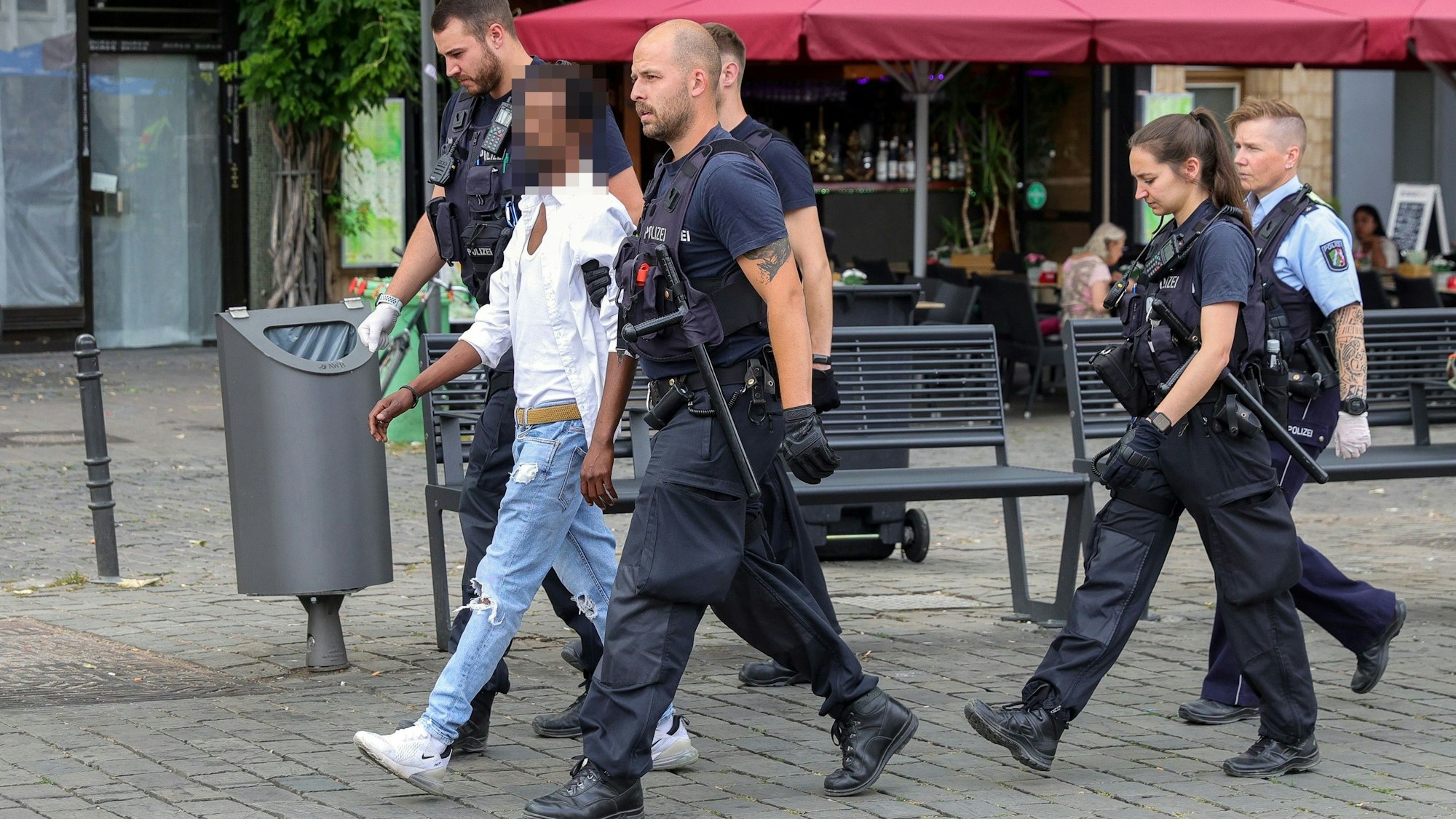 Polizisten führen einen mutmaßlichen Handydieb auf dem Kölner Heumarkt ab.