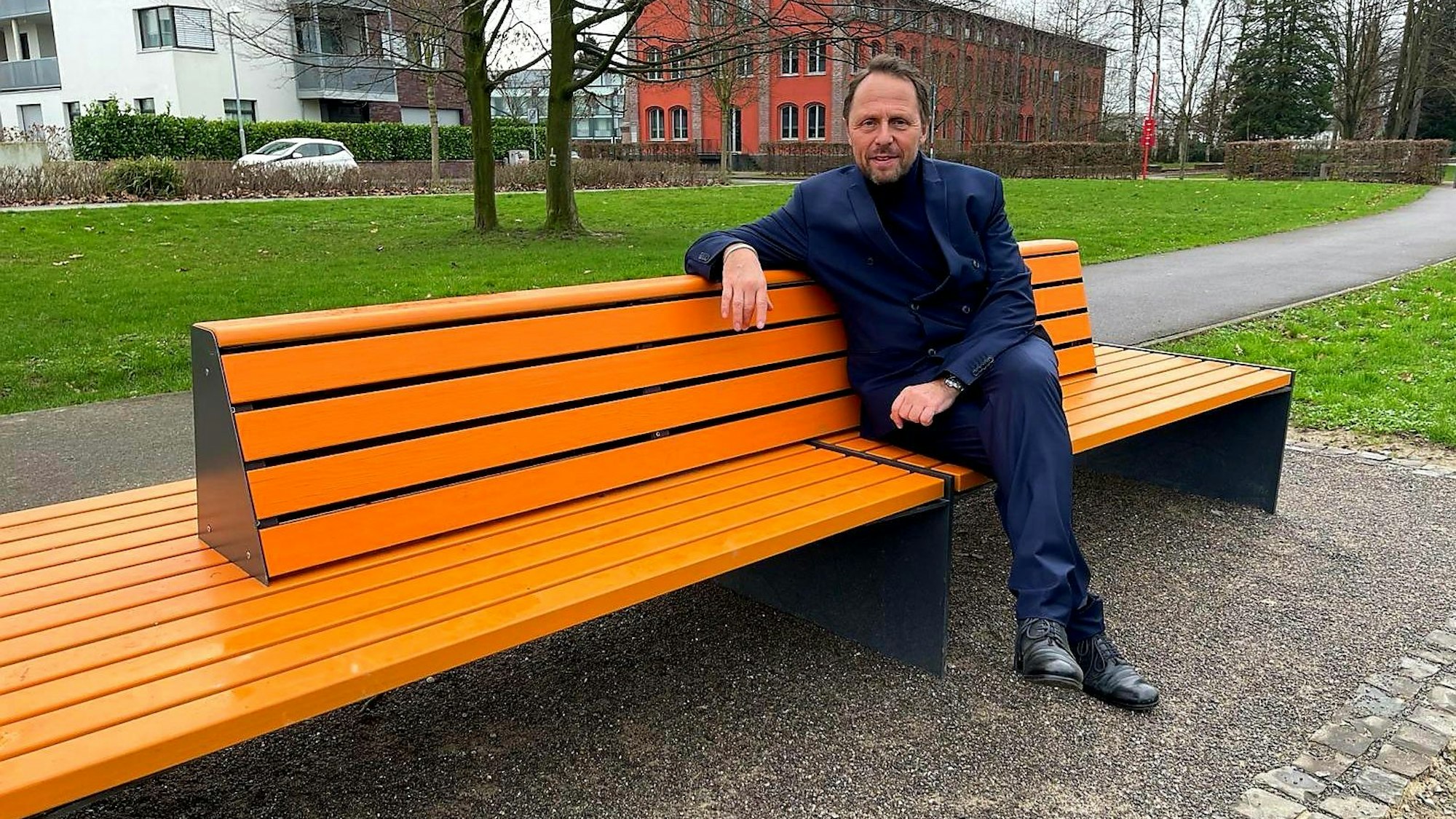 Der Leverkusener OB (Oberbürgermeister) Uwe Richrat (SPD) sitzt auf der vom Zonta-Club Leverkusen aufgestellten orangenen Bank in der Neuen Bahnstadt Opladen, auf der Susanne Wedewer ihn (und demnächst andere bekannte Menschen der Stadt) zum Thema Frauenrechte, Gleichstellung, Sexismus, Gewalt gegen Frauen befragte.