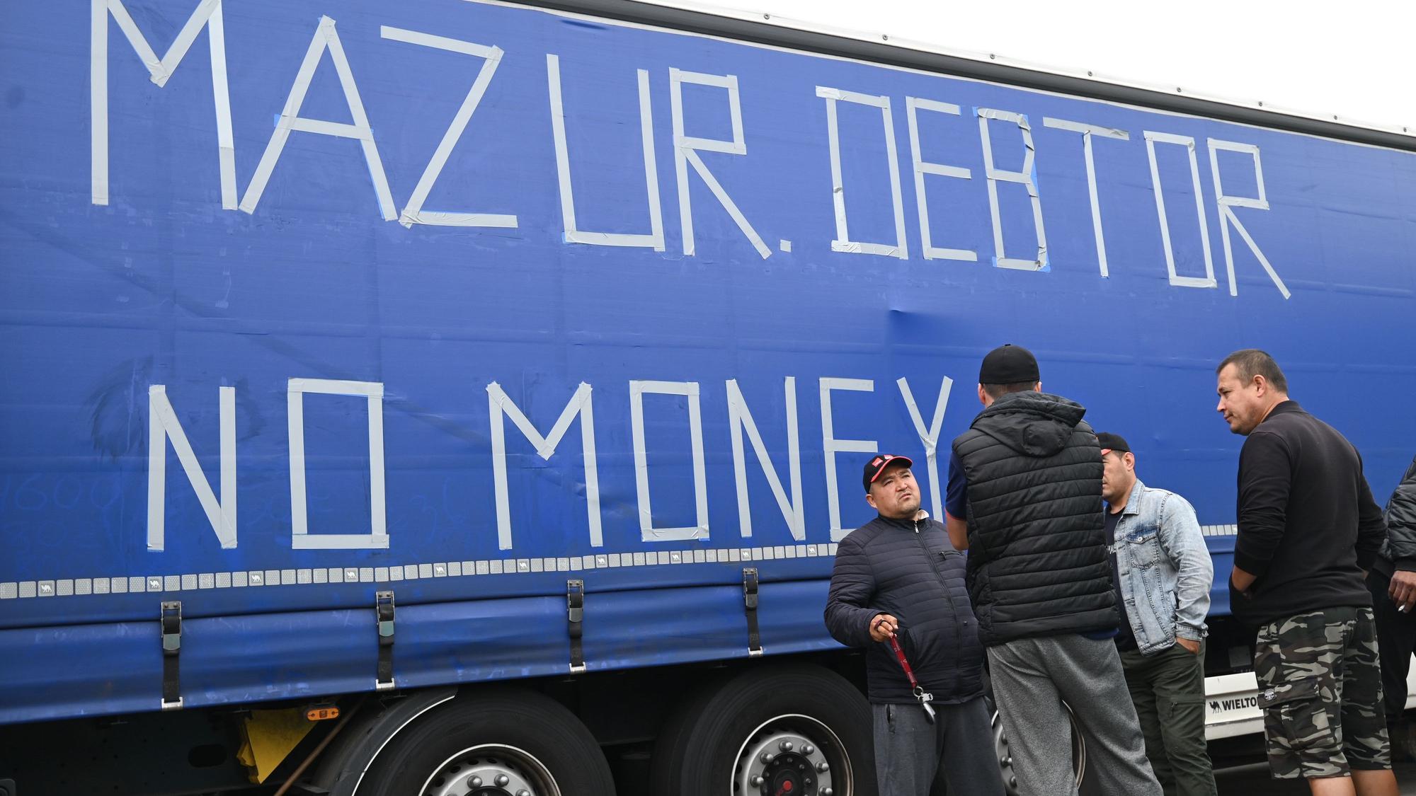 Osteuropäische Lkw-Fahrer stehen an einem Anhänger, auf dessen Plane die Worte «Mazur Debtor No Money» mit Klebeband aufgeklebt sind. Seit fast sechs Wochen streiken die Fahrer eines polnischen Speditionsunternehmens aus Usbekistan, Georgien und anderen Staaten Osteuropas und Zentralasiens auf der südhessisischen Raststätte. Die Männer fordern ausstehenden Lohn. (zu dpa «Europaparlamentarierin bei streikenden Fahrern: mehr Kontrollen nötig») +++ dpa-Bildfunk +++