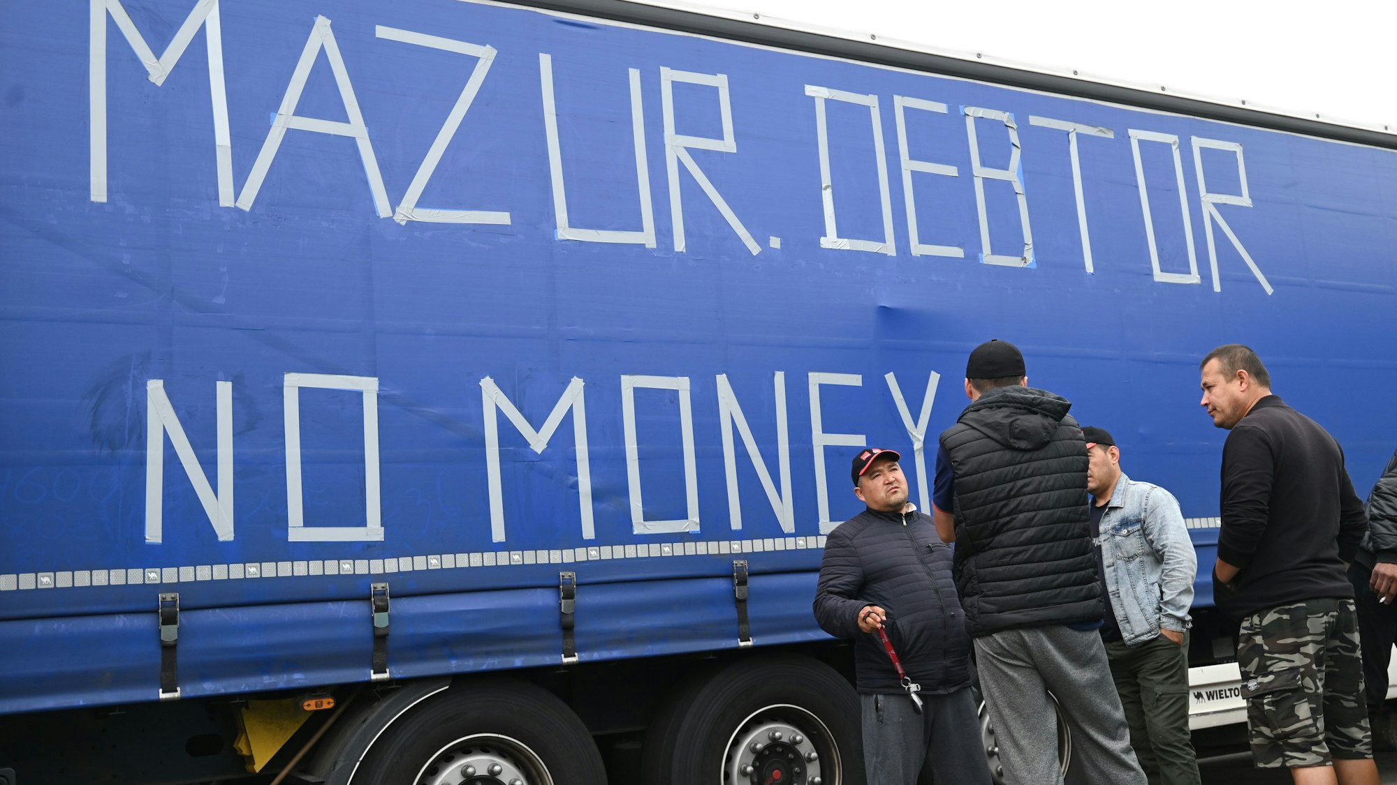 Osteuropäische Lkw-Fahrer stehen an einem Anhänger, auf dessen Plane die Worte «Mazur Debtor No Money» mit Klebeband aufgeklebt sind. Seit fast sechs Wochen streiken die Fahrer eines polnischen Speditionsunternehmens aus Usbekistan, Georgien und anderen Staaten Osteuropas und Zentralasiens auf der südhessisischen Raststätte. Die Männer fordern ausstehenden Lohn. (zu dpa «Europaparlamentarierin bei streikenden Fahrern: mehr Kontrollen nötig») +++ dpa-Bildfunk +++