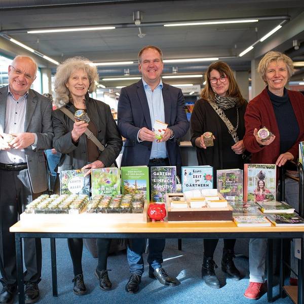 Drei Frauen und drei Männer lächeln in die Kamera, sie stehen hinter einem Tisch, auf dem Saatgut liegt.