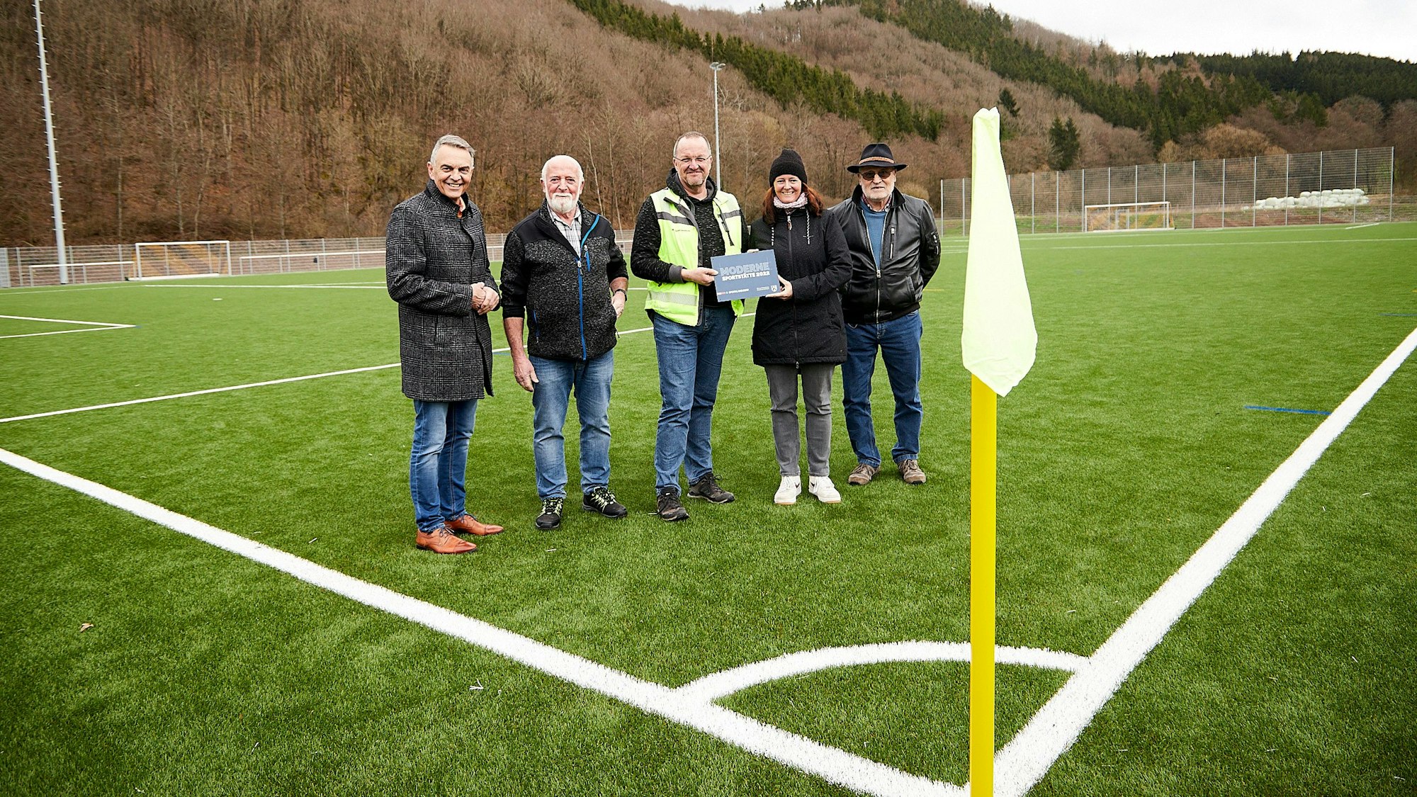 Rudolf Westerburg (v.l.), Peter Bauer, Markus Rodenbüsch, Ariane Gehlen und Norbert Klinkhammer stehen nebeneinander auf dem neuen Kunstrasenplatz. Vorne ist ein Eckfähnchen zu sehen.