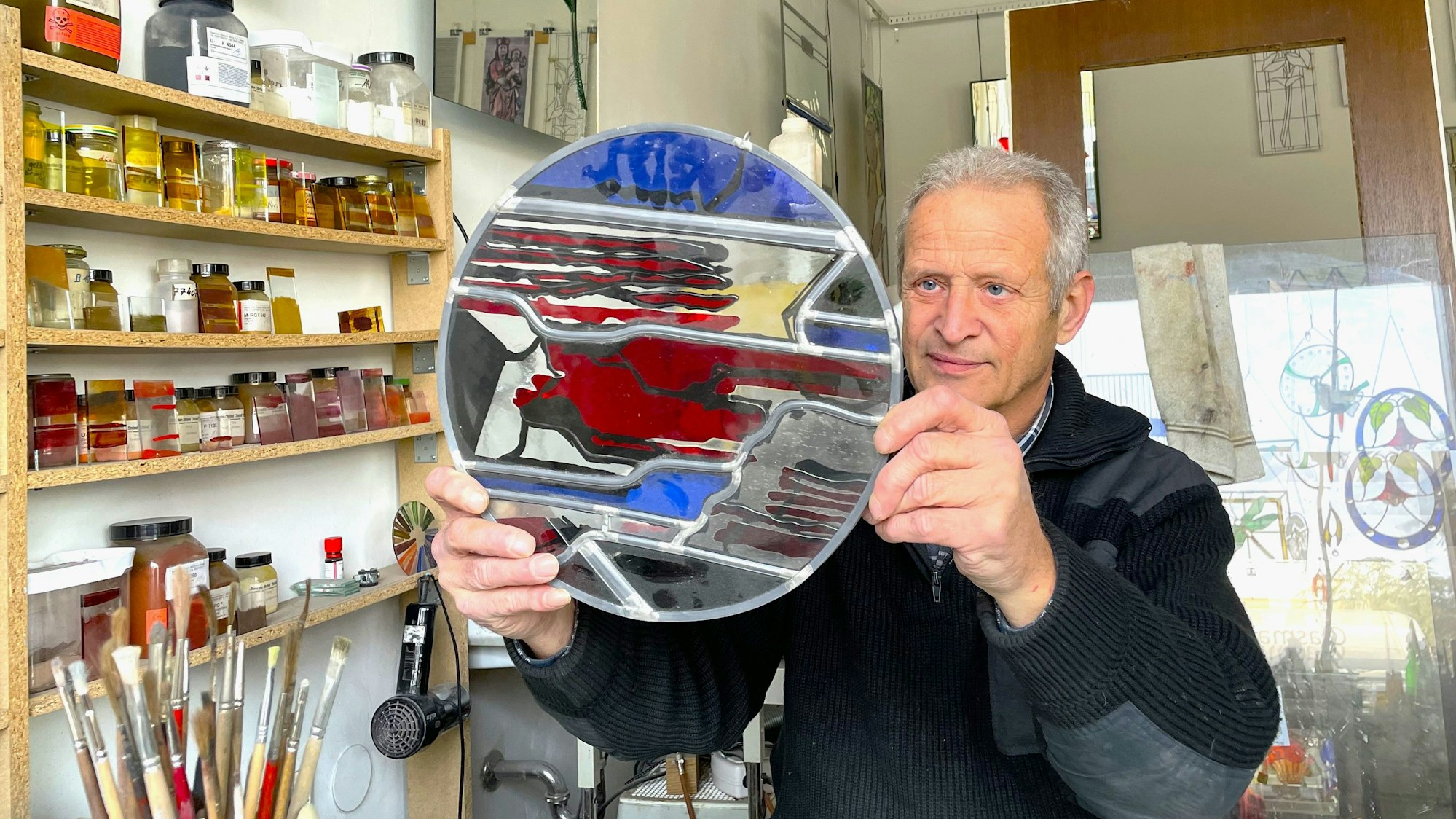 Ein Mann hält ein rundes bleiverglastes Objekt in den Händen und begutachtet es.