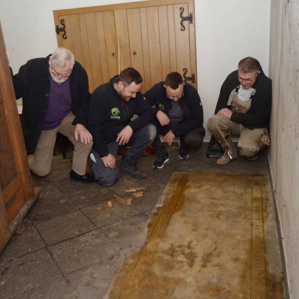 Die vier Männer hocken nebeneinander und schauen sich die Grabplatte an, links die Rückwand des Beichtstuhls.