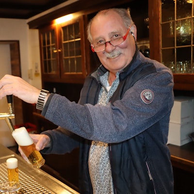 Ein Mann steht hinter der Theke am Zapfhahn und zapft ein Glas Kölsch.