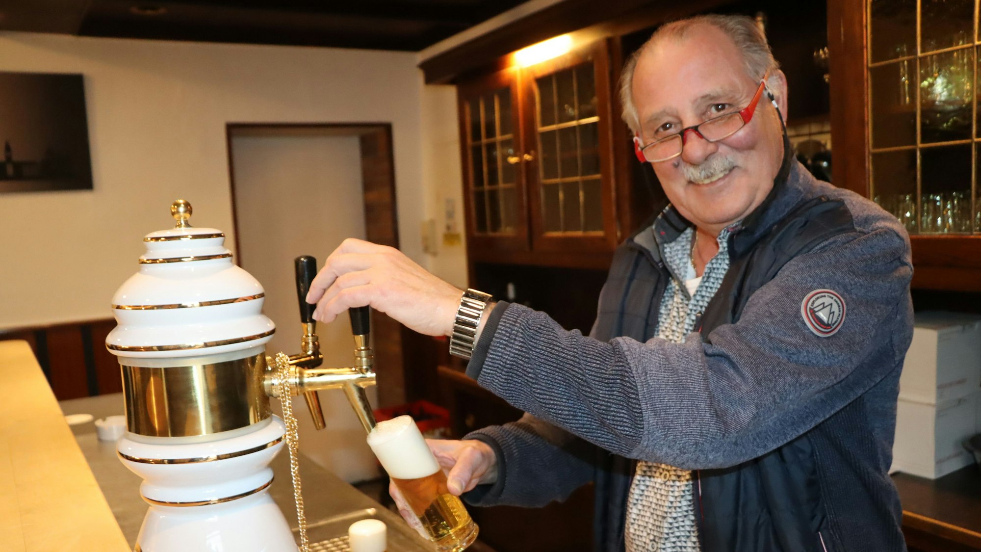 Ein Mann steht hinter der Theke am Zapfhahn und zapft ein Glas Kölsch.